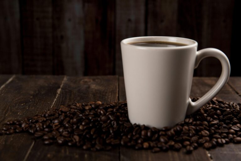 A rustic ceramic mug filled with hot coffee, surrounded by coffee beans on a wooden table.